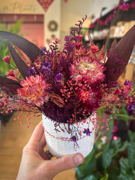 Bouquet of pink and purple flowers in a white vase held by a hand.